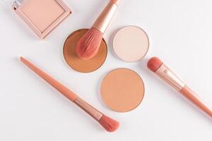 A few blocks, a refill of compact powder in different tones and a set of makeup brushes on a white background. Flat geometric lay. top view. photo