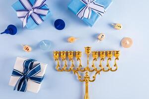 Fried donut with powdered sugar and jam on a plate, candles, minor, dreidels, gold coins on a blue background. The concept of the Hanukkah. photo