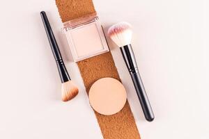 A pack of compact powder of a natural tone, a round block, a refill of a beige tone lie on a trace of dark dry powder. Two makeup brushes. top view. photo