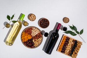 Two wooden trays with a mix of dried fruits and nuts, two bottles of red and white wine, glasses of wine, green tree branches. Tu be shvat. top view photo