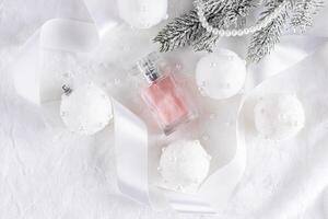 A beautiful bottle of pink perfume lies among the New Year's white balls on a mechanical background with a satin ribbon and a spruce branch. top view. photo