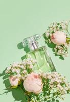 An elegant bottle of women's perfume with a light floral fragrance on a green delicate background with flowers. The top vertical view. A copy space. . photo