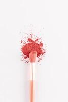 A beautiful makeup brush is lying on a sample of dry scattered blush in a pink tone on white background. The top vertical view. decorative cosmetics. photo