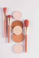 Beautiful cosmetic background with a set of beige makeup brushes and some round blocks, a refill compact powder in various tones. vertical. flat lay photo