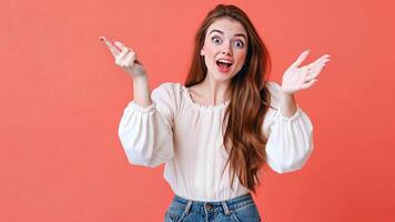 Curious young woman in a white blouse pointing to her left with a look of wonder against a coral background, expressing engagement and brightness. Copyspace video