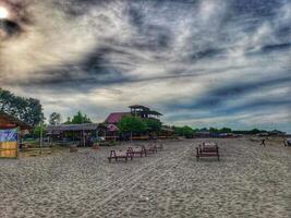 A beach with benches and a building under a cloudy sky photo