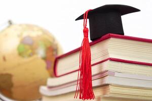 A Graduation cap placed on a stack of books and blurred globe behind. It is the concept of education, knowledge, learning and successful. photo
