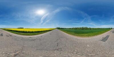 spherical 360 hdri panorama on old asphalt road with cracks near rapeseed canola colza fields with clouds on blue sky in equirectangular seamless projection photo