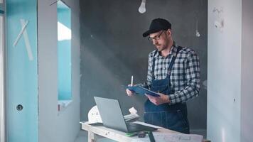 Man standing in front of a laptop on a table while holding a clipboard video