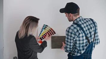 A woman designer and a builder contractor select materials for finishing the room and the color of the walls. Work on a construction site using palettes and samples of materials. Apartment video