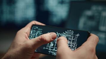 The shows male hands holding a smartphone and working on a laptop with building plans or blueprints displayed on the screens. The architect is working on a project. video