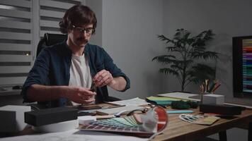 A stylish male architect is working on creating a project. The specialist is sitting at his workspace designing the interior. The worker is using blueprints, palettes, material samples, and textures. video