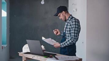 A construction engineer at a construction site works with projects using a laptop and blueprints. A man is responsible for finishing works and architectural solutions video