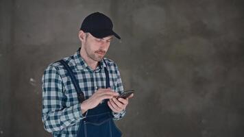 A man in a construction uniform uses a smartphone on a construction site. Working with modern technologies and the Internet. video