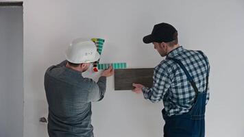 The developer, architect and builder select materials for finishing the apartment. A male builder holds a sample of porcelain tiles, an architect selects the color of the walls. video