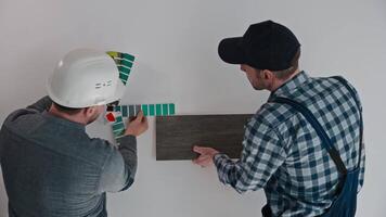 The developer, architect and builder select materials for finishing the apartment. A male builder holds a sample of porcelain tiles, an architect selects the color of the walls. Construction video
