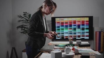 A woman interior designer is creating a mood board. The specialist is using palettes, as well as texture and material samples. The woman is working in a design studio. The office video