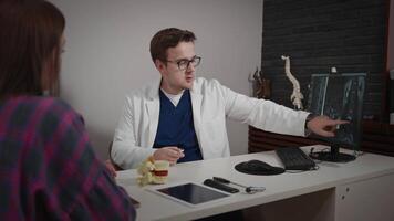 An experienced doctor, osteopath, conducts consultations in a modern clinic. A man consults a patient. The MRI image is open on the computer screen. video