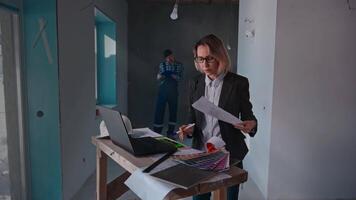 The developer's company specialists work at the construction site. A woman architect uses a laptop and drawings. A male builder takes measurements of a room. video