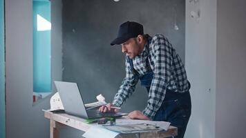 A male contractor builder at a construction site, working with a project on a laptop. An engineer is using blueprints to plan construction work. video