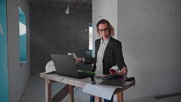 A woman interior designer is working on creating a design project at a construction site. The specialist uses a laptop, drawings and palettes to find the style of the room. video