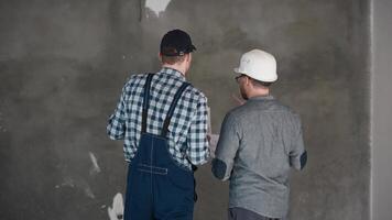 two construction workers are standing next to each other in front of a wall video