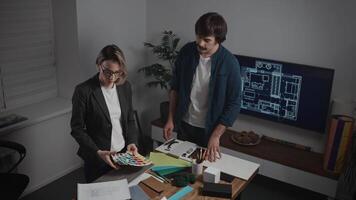 An architectural bureau. Colleagues, a man and a woman, are working on creating an interior design. The designers have laid out various textures, palettes, and material samples on the table video