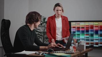 Sharing a desk, a man and a woman are in front of a laptop for an event video