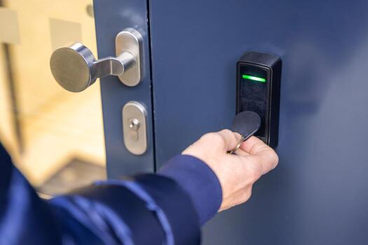 Close up view of person using a electric lock key fob to access a building via a reader of entry system mounted on a house wall. High quality photo