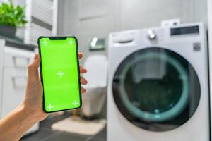 Young woman using mobile phone control via wi-fi and app for washing machine in home. Homesmart app, chroma key green screen. High quality photo