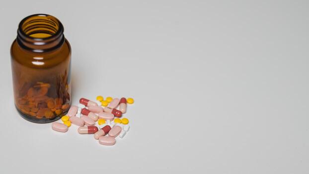Of colorful pills spilled from an amber bottle, an array of medication types on clean, light background Ideal for health-related themes photo