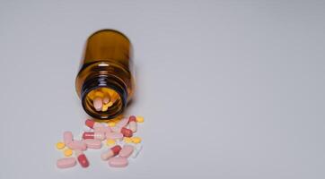 Close-up view of brown bottle tipped over, spilling colorful pills and capsules onto smooth surface, highlighting importance of medication safety and awareness photo
