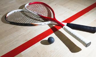 Two rackets and two squash balls lie on the parquet floor. Horizontal photo