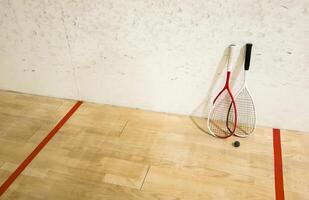 Two rackets and two squash balls lie on the parquet floor. photo