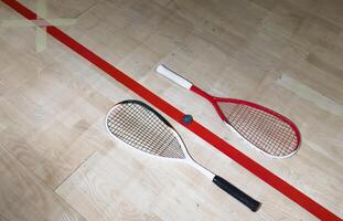 Two rackets and two squash balls lie on the parquet floor. Horizontal photo