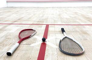 Two rackets and two squash balls lie on the parquet floor. photo