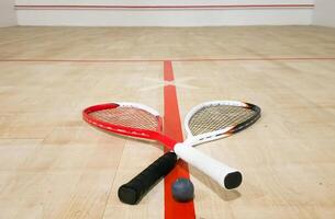 Two rackets and two squash balls lie on the parquet floor. photo