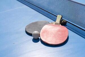Two table tennis or ping pong rackets and ball on blue table with net photo