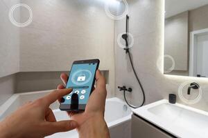 Internet of things. Focus on modern smartphone with blank mockup screen for smart home control system interface in young female customer user hand. Blurred living room interior on background. Close up photo