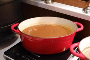 red pot filled with a creamy soup or sauce, sitting on a stovetop photo