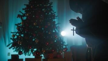 Man Prays With Crucifix In Front Of Christmas Tree In Silhouette photo