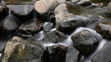 Large rocks are scattered along the stream, with gentle water flowing over them, creating a calming natural view. Long Exposure photo