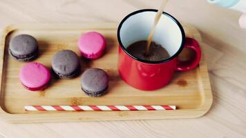Pouring hot cocoa into a red mug, against the background of a wooden tray and small macaroons video