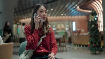 Woman on Phone in Cafe.A focused woman in a red sweater sits in a modern cafe, engrossed in a phone call. The bustling atmosphere of the cafe creates a sense of energy and connection. video