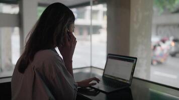 Woman engrossed in work, multitasks on her laptop and phone, showcasing dedication and efficiency in a modern setting. video