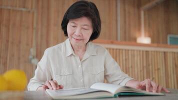 Close-up of senior woman sitting reading a paper book at a table with fruits on it. Young woman searching for information on the pages of a book. Hobby, learning and relaxation. video