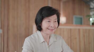 Close up of senior asian woman looking at laptop screen and taking notes in bamboo house for learning and researching online. Self development, digital connection video