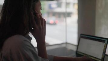 Woman engrossed in work, multitasks on her laptop and phone, showcasing dedication and efficiency in a modern setting. video