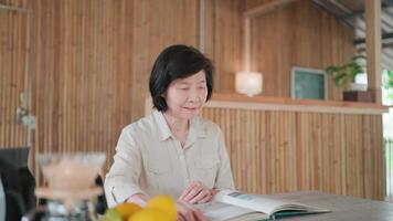 Senior woman sitting at table reading paper book with coffee dripper and fruits placed inside bamboo house, searching information on book page, hobby, learning and relaxation, self development concept video