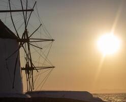 Traditional windmills with white walls and wooden structures at sunset in Mykonos, Greece. Historical architecture and travel concept. photo
